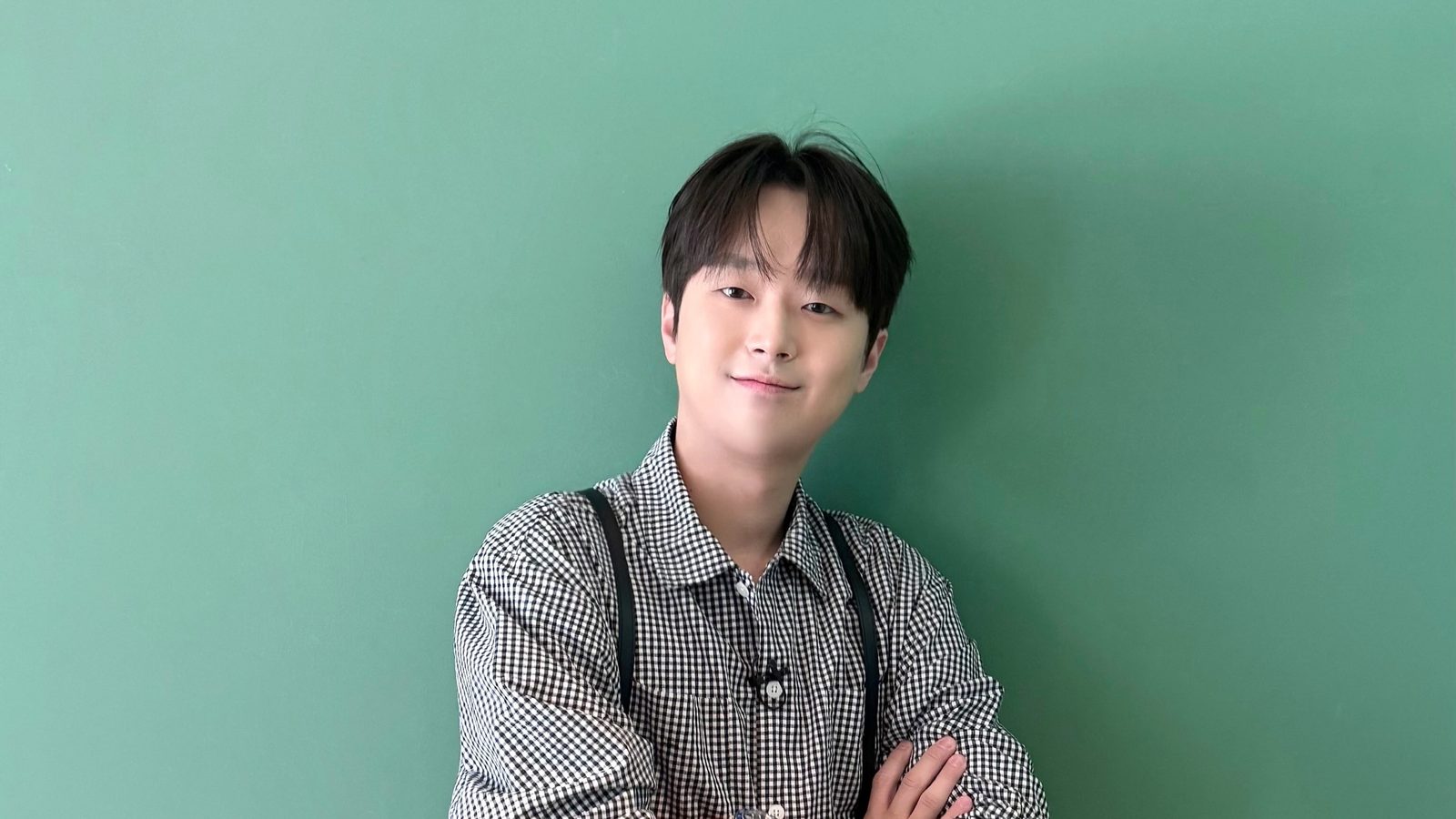 체크무늬 셔츠 차림으로 팔짱을 끼고 미소 짓는 이찬원의 상반신 사진