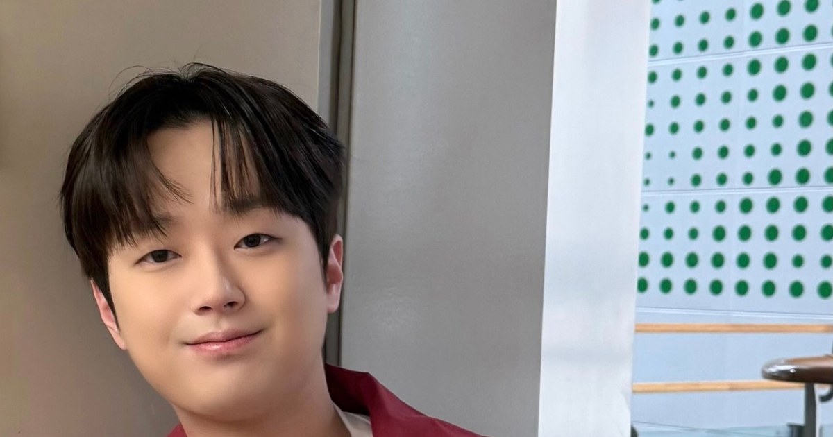 이찬원이 붉은 재킷을 입고 복도 벽 앞에서 미소 짓는 모습