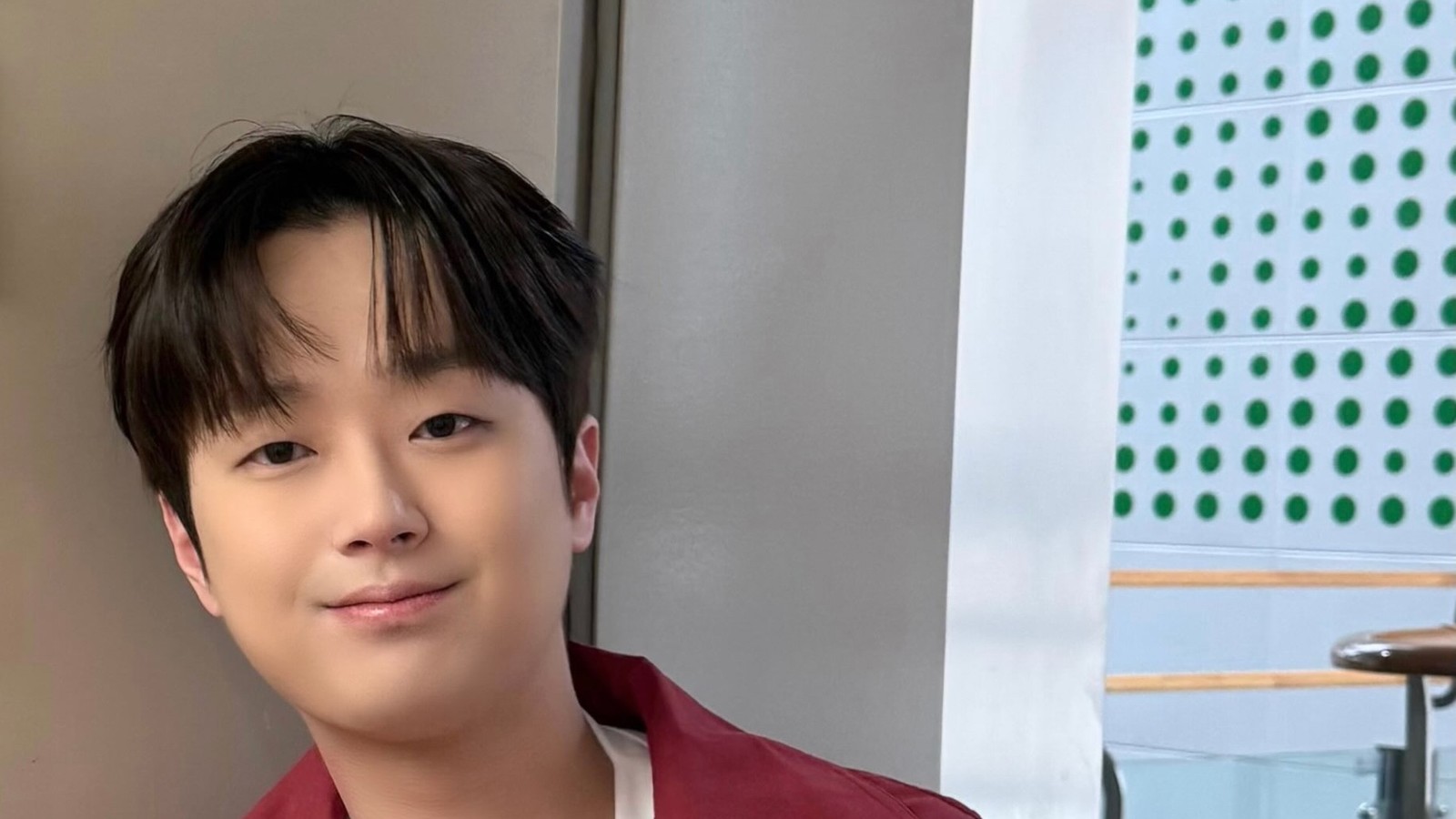 이찬원이 붉은 재킷을 입고 복도 벽 앞에서 미소 짓는 모습