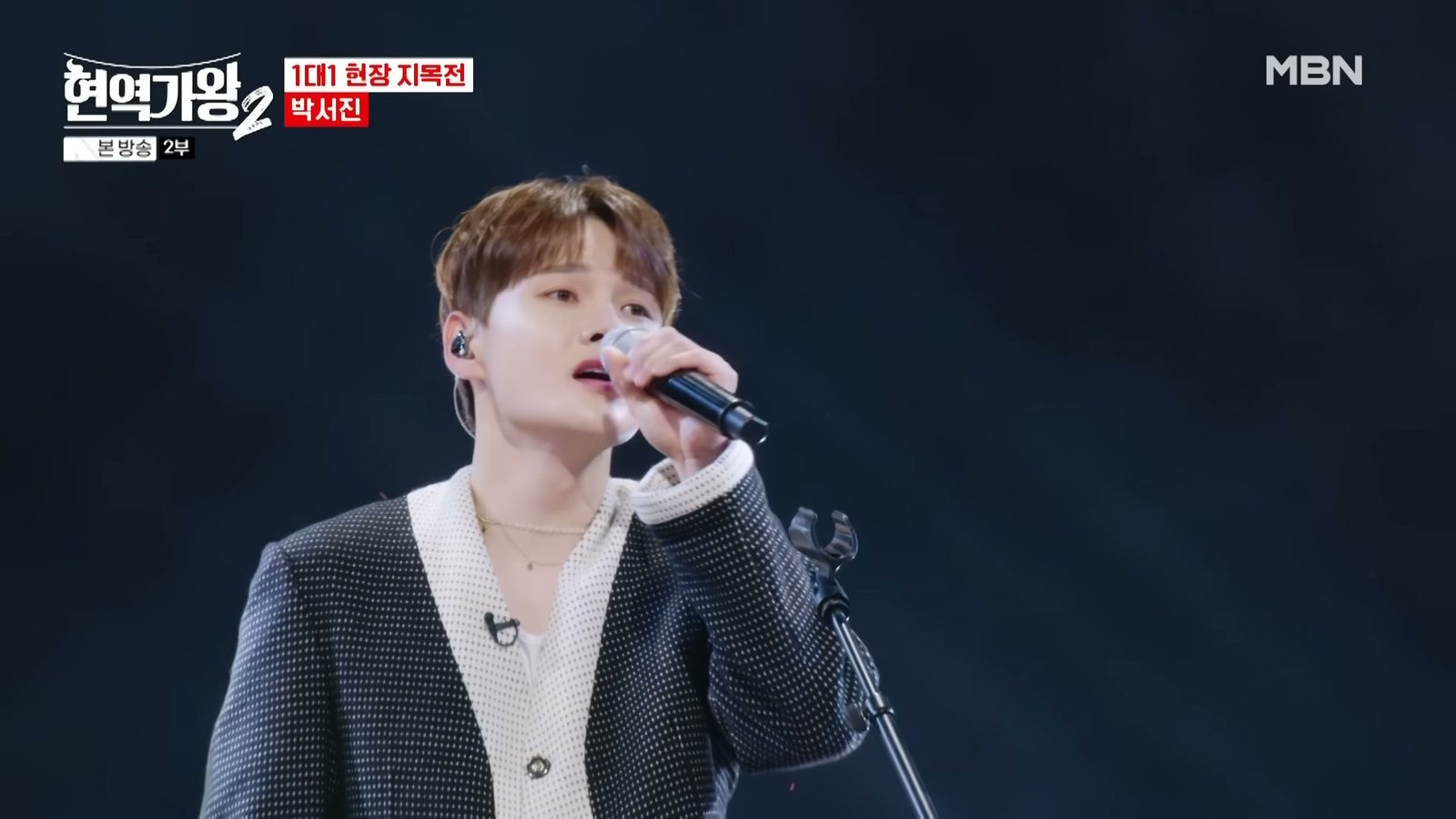 박서진이 어두운 무대에서 마이크를 쥐고 노래하는 모습