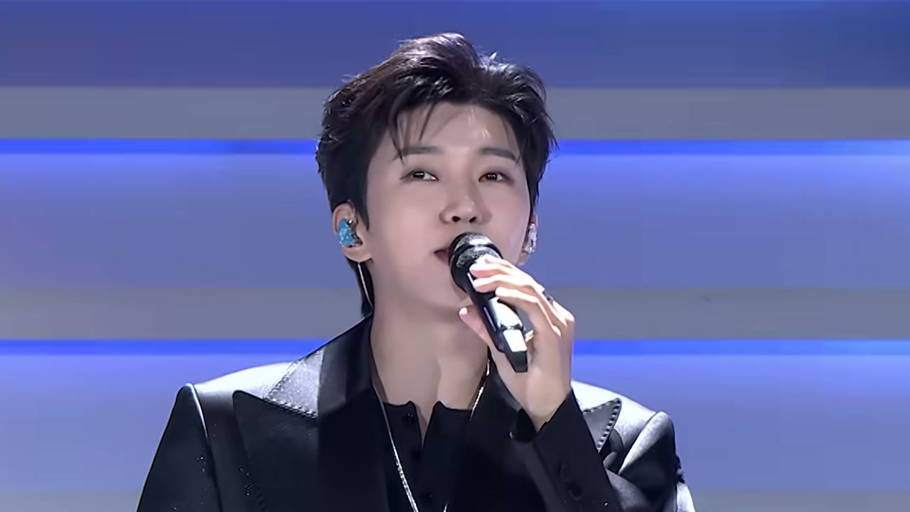 임영웅이 검은 재킷 차림으로 마이크를 들고 노래하는 모습, 임영웅 공식 유튜브 'Baila' 라이브 클립 장면