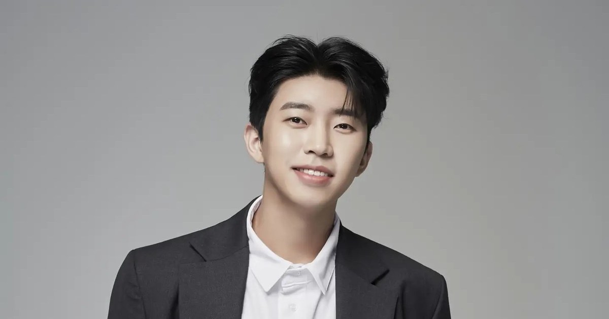 회색 배경 앞에서 짙은 재킷과 흰 셔츠를 입고 웃는 임영웅