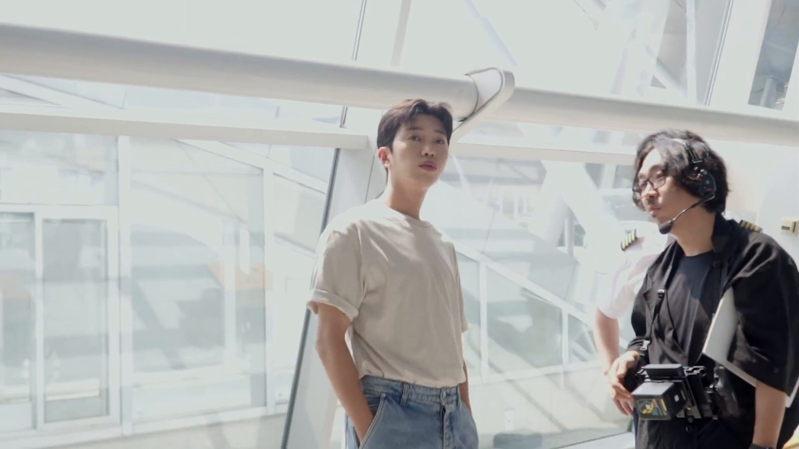 베이지색 티셔츠를 입은 임영웅이 공항 유리 벽 앞에서 스태프와 이야기하는 모습