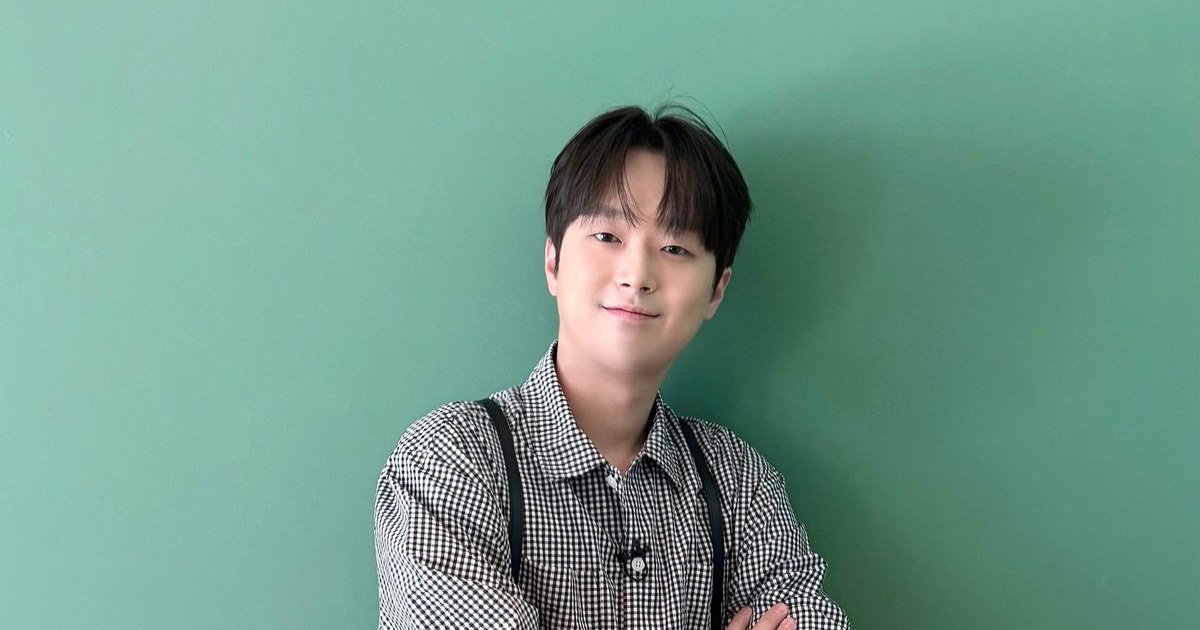 체크무늬 셔츠 차림으로 팔짱을 끼고 초록 벽 앞에서 미소 짓는 이찬원