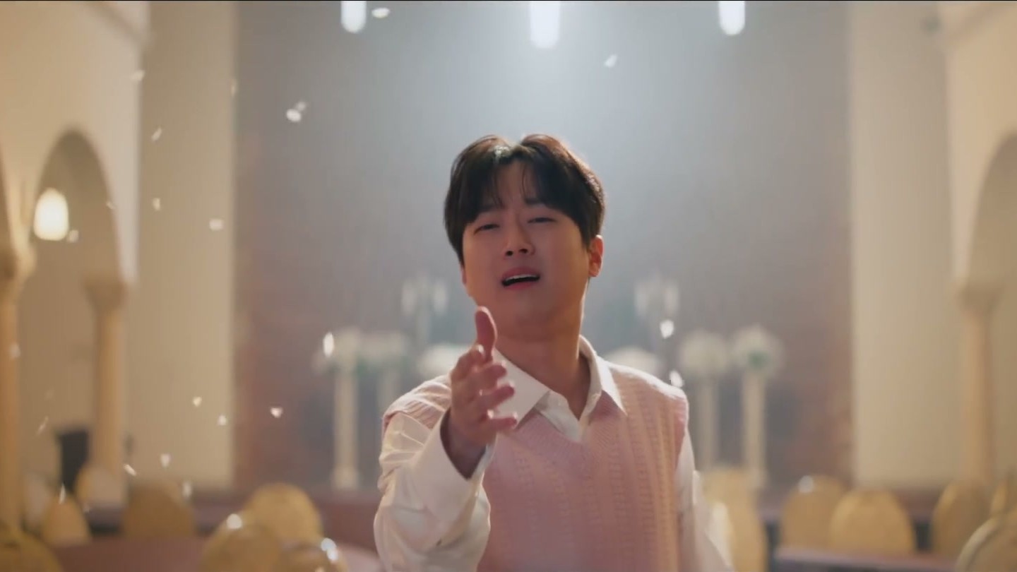 분홍 니트 조끼를 입은 이찬원이 꽃잎이 날리는 홀에서 한 손을 내밀며 노래하는 모습
