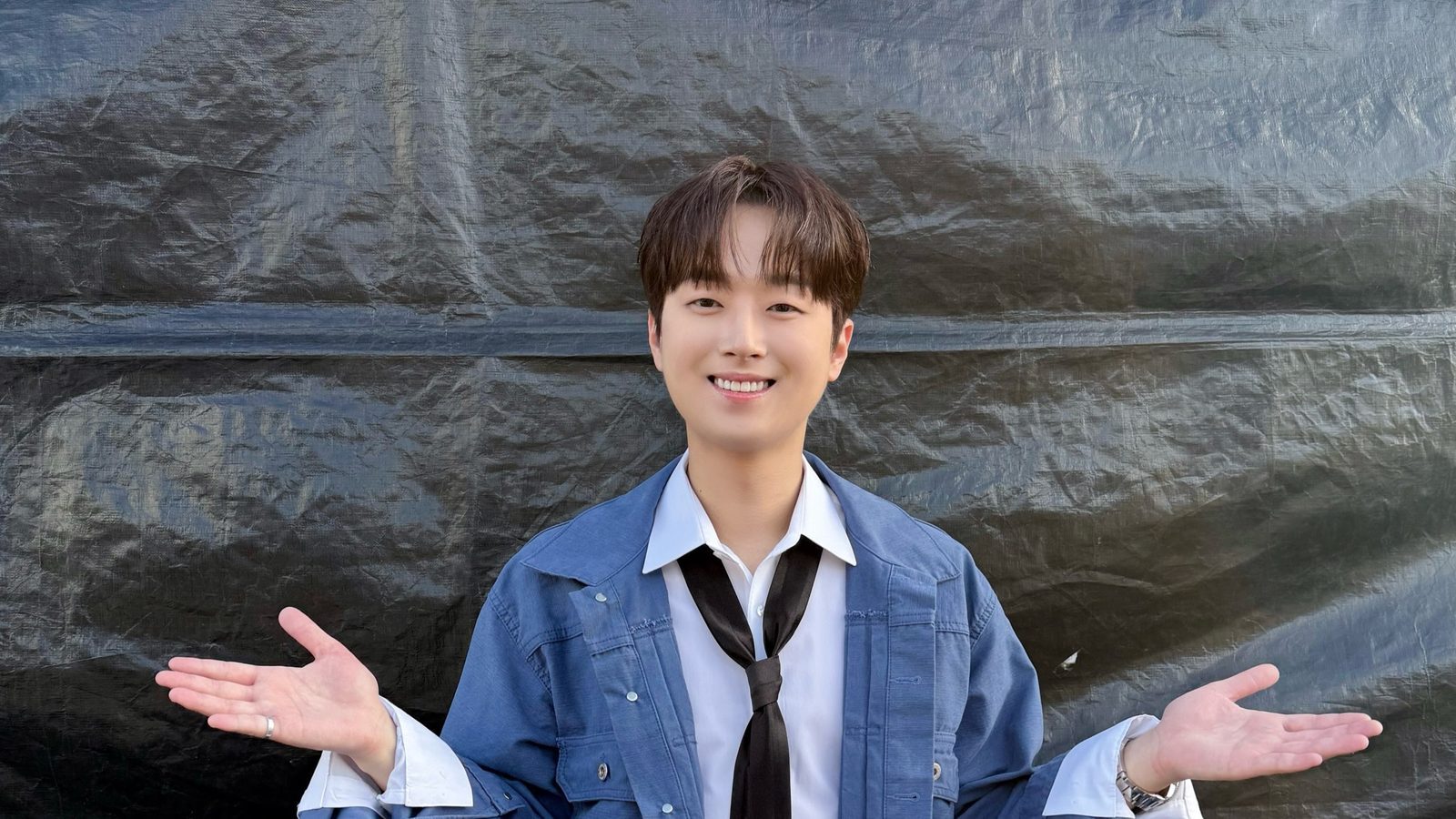 청색 데님 재킷에 넥타이 차림으로 두 팔을 벌리고 웃는 이찬원