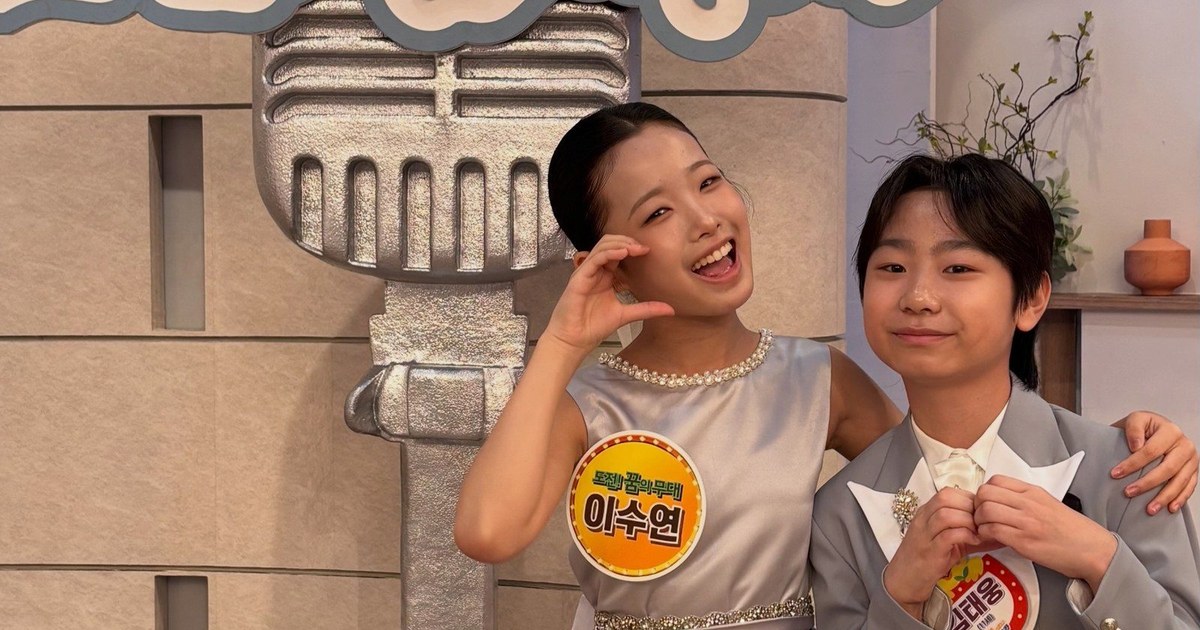 회색 원피스 차림의 이수연이 환하게 웃으며 회색 재킷을 입은 김태웅과 '아침마당' 세트 앞에서 어깨동무한 모습