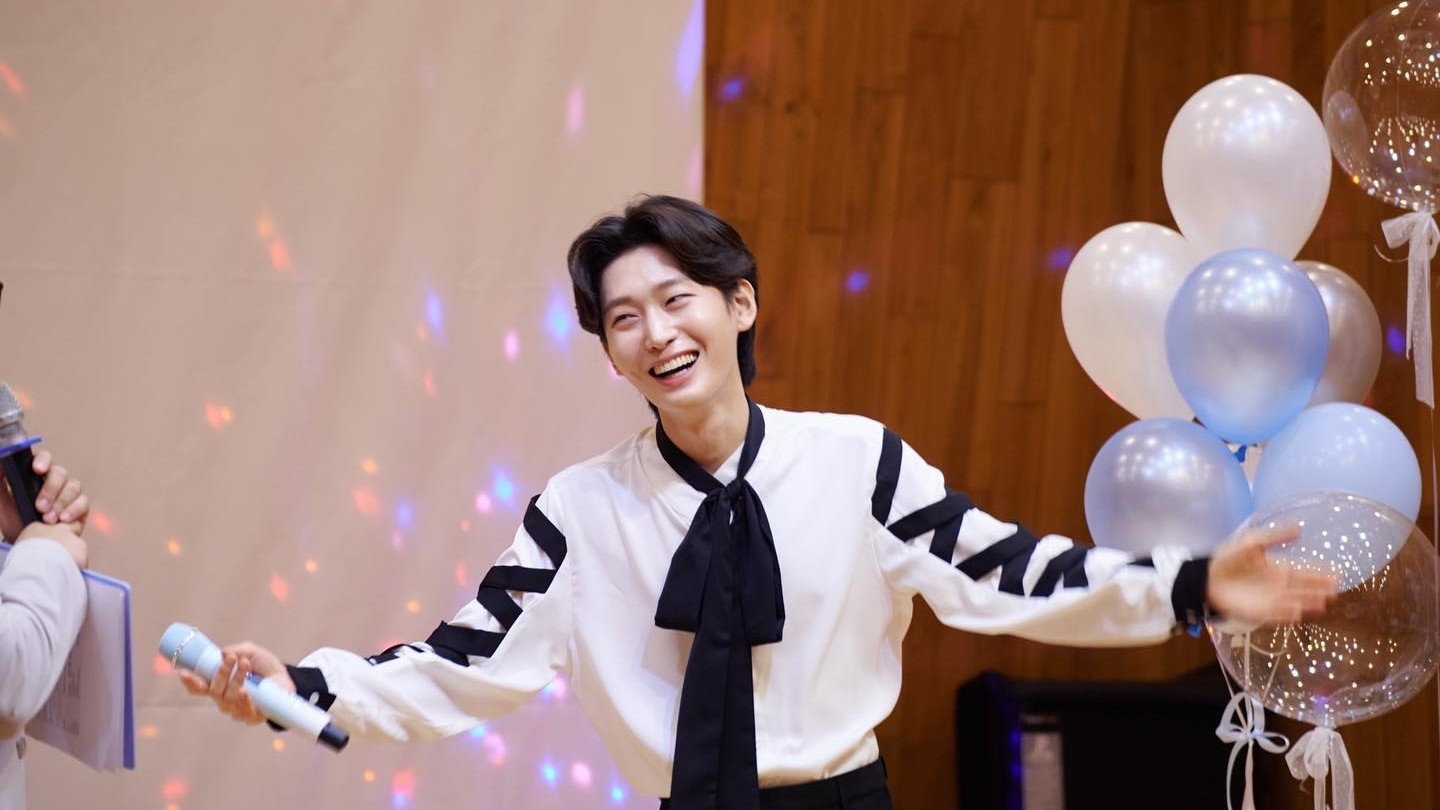 풍선 앞에서 흰 셔츠에 검은 리본 차림의 김용빈이 마이크를 들고 활짝 웃는 모습