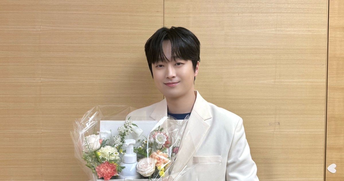 흰 재킷을 입고 꽃다발을 든 채 부드럽게 웃는 이찬원