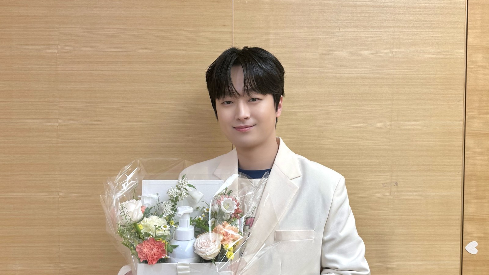 흰 재킷을 입고 꽃다발을 든 채 부드럽게 웃는 이찬원