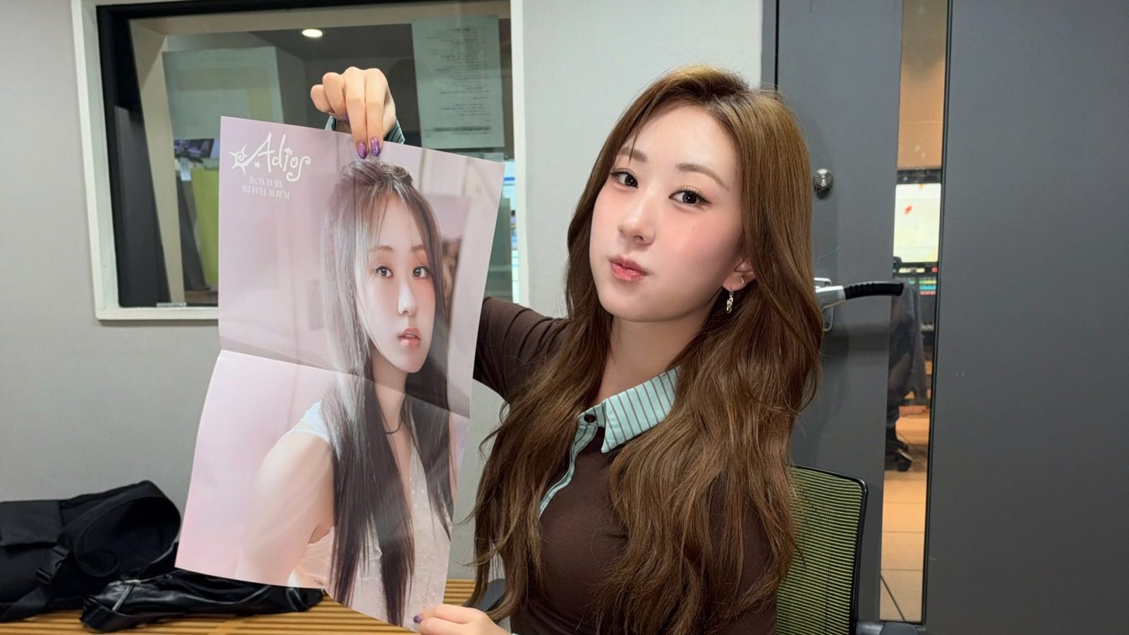 'Adios' 앨범 포스터를 들어 보이며 카메라를 바라보는 전유진