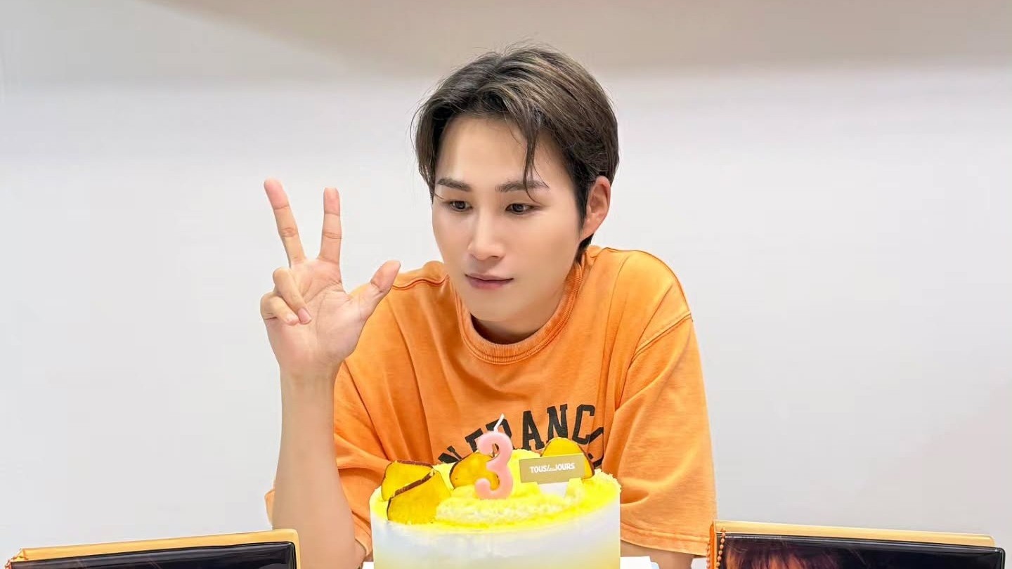 주황색 티셔츠 차림으로 브이를 하며 케이크를 바라보는 김희재